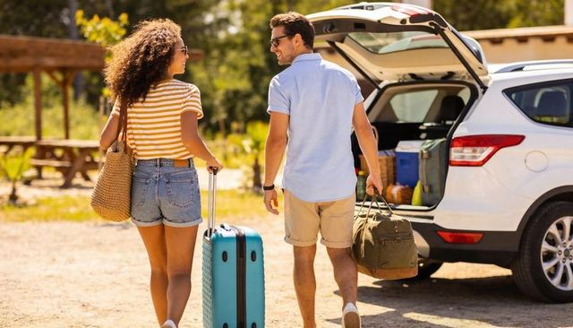 Couple walking toward suv with luggage at sunny campsite for summer road trip getaway