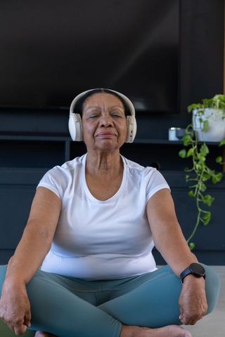 Senior african american woman meditating at home wearing headphones and smartwatch