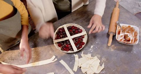 Assembling cherry tart with pastry lattice on flour-dusted counter, hands placing strips