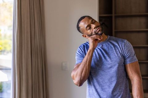 Mature african man resting jaw stretching neck sunlit home interior quiet contemplation