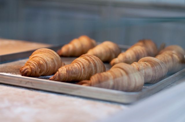Freshly baked croissants cooling on baking tray in a bakery. Ideal for depicting concepts related to breakfast, baked goods, artisanal baking, or European cuisine. Perfect for use in culinary blogs, restaurant websites, and cooking magazines.