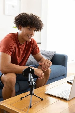 Young man recording podcast at home with microphone and laptop