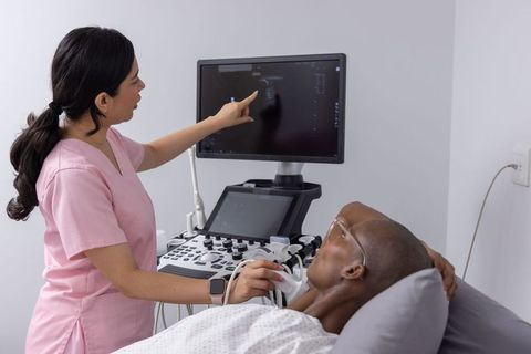 Hispanic sonographer performing bedside thyroid ultrasound on senior african american man