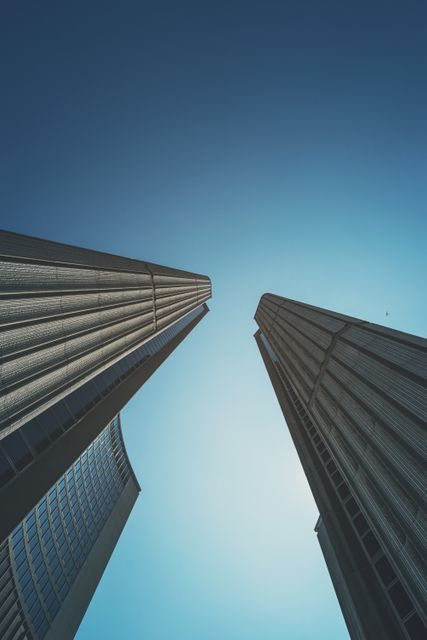 Two modern skyscrapers are seen from a low angle with a clear blue sky in the background. Perfect for use in articles and advertisements related to architecture, urban living, business districts, construction, commercial properties, and real estate development.