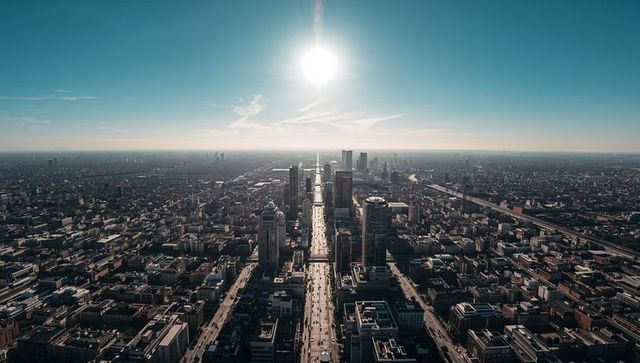 Sunlit avenue stretching toward horizon through dense downtown skyline, aerial cityscape