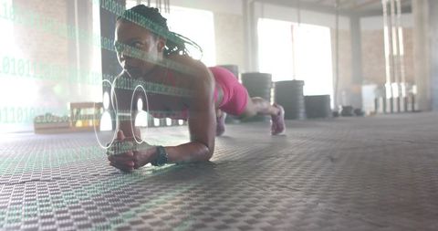Female athlete performing forearm plank in loft gym with wearable fitness data overlay