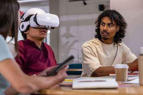 Diverse team testing virtual reality headset while collaborating over tablet and notes