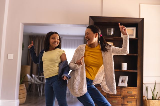 Happy asian mother and daughter having fun together dancing in living room at home, copy space. Domestic life, family, togetherness, relaxation, inclusivity and lifestyle.