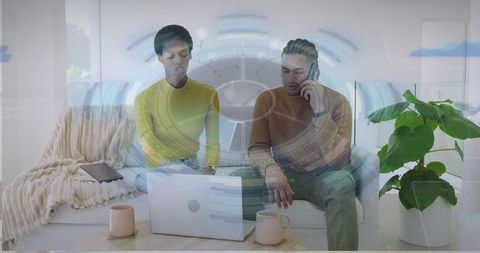 Remote coworkers collaborating on laptop in modern living room with coffee mugs and plant