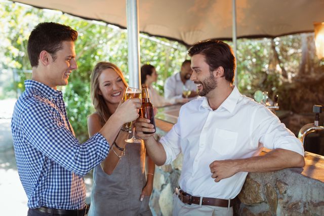 Smiling friends toasting glass and bottle of alcohol at counter in restaurant