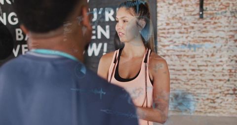 Young woman discussing workout with trainer in brick gym holding jump rope during coaching