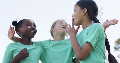 Smiling multicultural girls celebrating friendship in matching green t-shirts outdoors