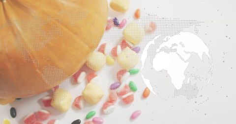 Autumn pumpkin surrounded by colorful halloween candies with halftone world map overlay