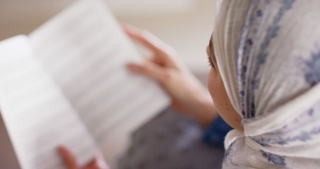 This image features a close-up shot of a Muslim woman wearing a hijab while reading a book. Ideal for educational materials, cultural representation, religious studies, and articles or blogs focused on reading, learning, and knowledge acquisition. Suitable for illustrating concepts of concentration and study.