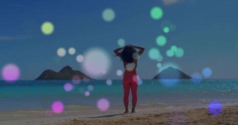 Standing woman facing turquoise sea with twin islets and dreamy colorful bokeh