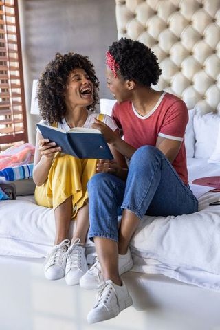 Two black women laughing and sharing journal on cozy bed