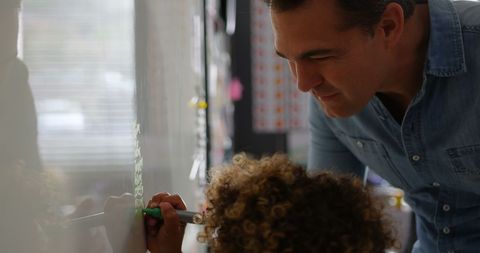 Male Teacher Guiding Young Student Writing on Whiteboard