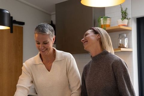 Senior woman and younger adult smiling while cooking together in modern cozy kitchen