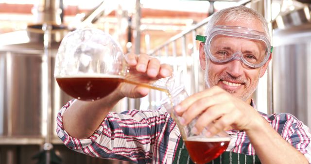 A skilled brewer wearing safety goggles and laboratory attire pours beer from a beaker into a measuring container. Ideal for content about the brewing process, craft beer production, or showcasing the brewing industry. Can be used in blogs, websites, or promotional materials related to breweries and beer making.