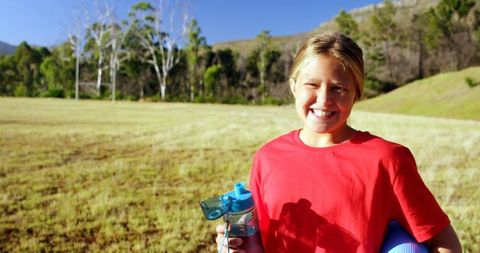 Smiling Girl Exercising Outdoors with Water Bottle and Yoga Mat
