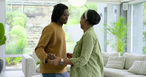 African American couple dancing and holding hands in sunlit modern living room