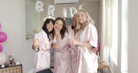 Joyful bride and bridesmaids toast before wedding in matching robes