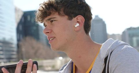 Young man speaking into smartphone wearing wireless earbud on urban rooftop