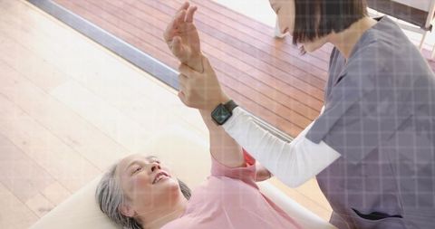Caregiver helping senior woman stretch arm during home therapy session with smartwatch