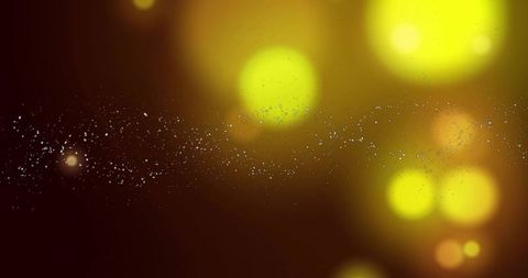 Glittering silver particle trail on dark gradient with yellow-green bokeh glow and warm orange orbs