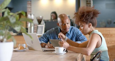 Young professionals collaborating over smartwatch and laptop at modern cafe