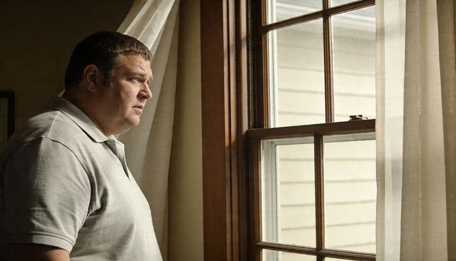 Pensive man gazing through wooden-framed window with sheer curtains and soft daylight