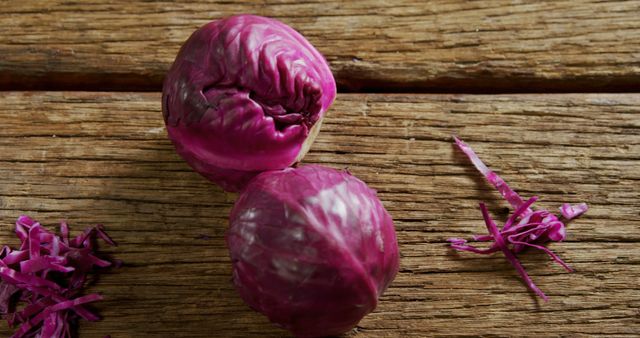 Two purple cabbages rest on a wooden surface, surrounded by shredded pieces, with copy space. Their vibrant color and rustic backdrop suggest a focus on healthy, organic produce or a cooking concept.