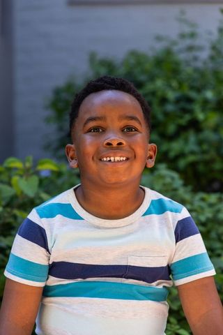 Smiling african american boy sitting in yard wearing striped t-shirt outdoor portrait