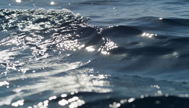 Sunlight glinting on ocean waves showing foamy crest, sparkling highlights and rippled surface