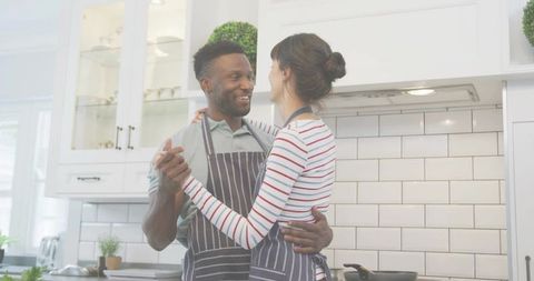 Couple dancing while cooking together in bright modern kitchen wearing striped aprons