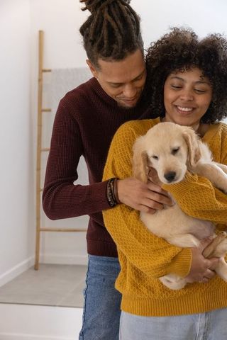 Couple holding golden retriever puppy, embracing new pet in cozy home