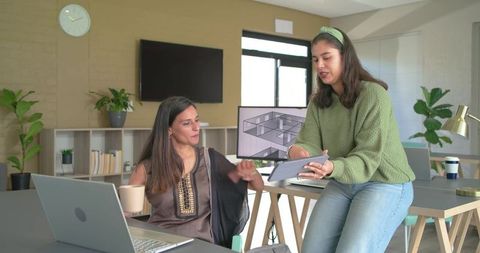 Indian and diverse women reviewing 3D floor plan on tablet and laptop in modern office