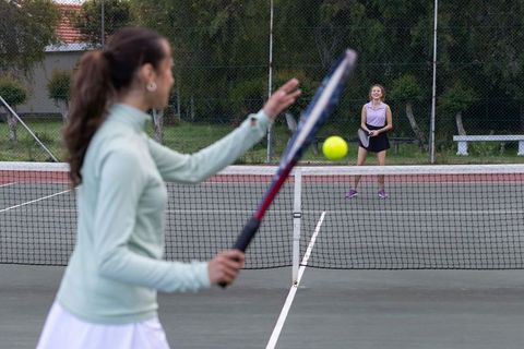 Women playing tennis on outdoor court hitting forehand over net during practice session