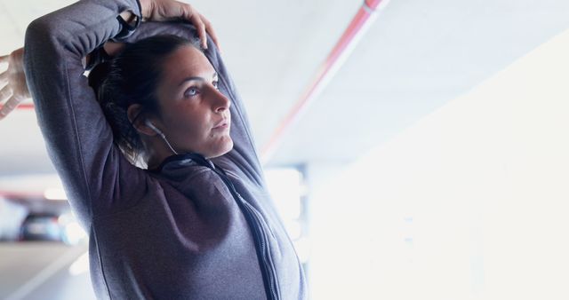 Woman in workout attire stretching in an urban parking lot, looking determined. Useful for fitness, exercise, health, and urban lifestyle content, as well as promoting active living and workout routines.