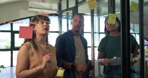 African american team brainstorming on glass wall with sticky notes and tablet