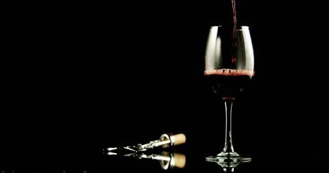Red wine pouring in glass with corkscrew on black background