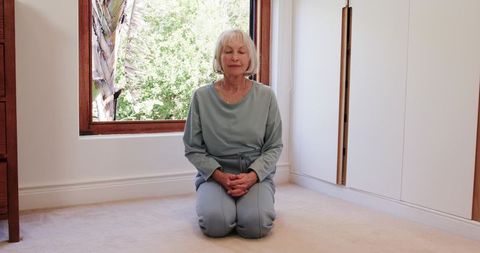 Senior woman meditating at home in natural light