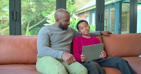 African american father and son reading tablet together on cozy leather sofa at home