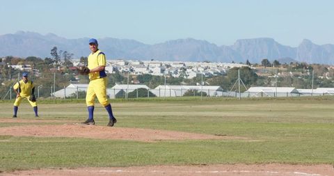 Pitcher and Infielder in Yellow Uniforms Pitching on Suburban Baseball Field with Mountain View