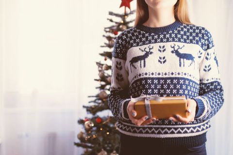 Cozy woman holding christmas gift near decorated tree