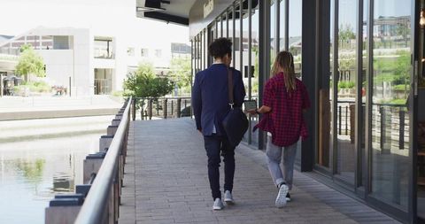 Two young men walking along waterfront promenade with storefront reflections