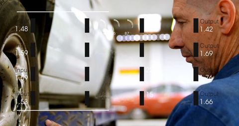 Mechanic inspecting lifted car wheel with digital overlay readouts in busy auto workshop