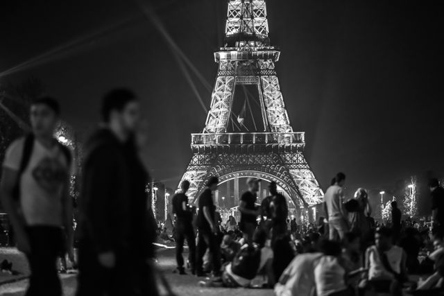 Tourists and locals gathering near Eiffel Tower at night. The tower is beautifully illuminated against the night sky. Perfect for themes related to travel, tourism, Paris landmarks, night celebrations, or world-famous structures and their appeal to both tourists and locals.