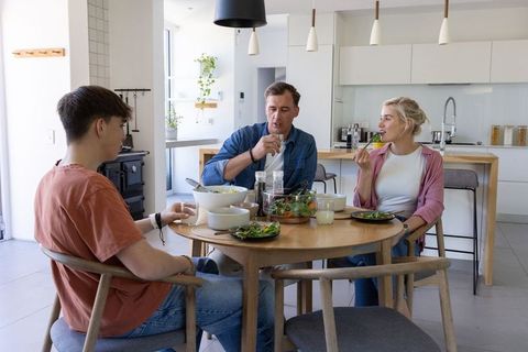 Modern family sharing healthy salad at round wooden dining table in bright open kitchen