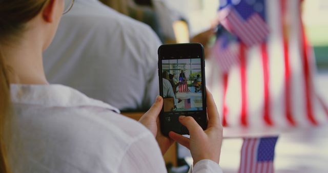 Person capturing a patriotic scene with an American flag on smartphone. Ideal for use in articles or media related to Independence Day, patriotism, technology, or social media engagement. Could illustrate the intersection of tradition and modern technology.